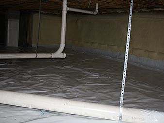 Plastic-lined crawlspace floor with pipes and a measuring rod.