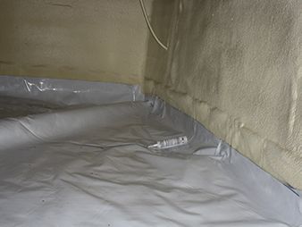 Plastic sheeting lining a corner of a room, with a gray tarp-covered floor and beige walls