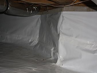 Crumpled silver plastic sheeting lining a crawlspace beneath exposed wooden beams and pipes