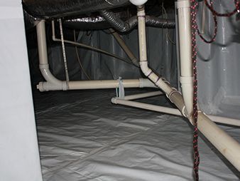 Under-sink plumbing pipes and hoses inside a cabinet with a gray liner.