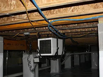 Underside of a house with exposed beams, cables, and a mounted HVAC unit on a support post