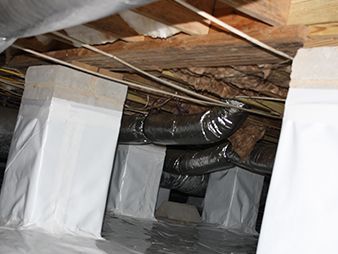 Crawlspace with insulated ducts and wrapped HVAC vents beneath wooden floor joists