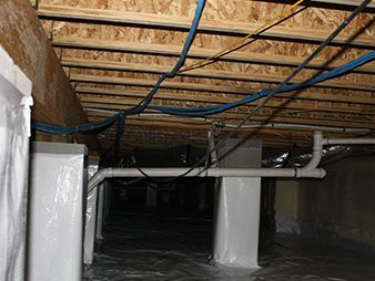 Basement crawlspace with exposed joists, blue cables, and white insulated pipes and columns