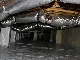 Crawlspace with silver insulated ducts overhead and plastic sheeting covering the floor.