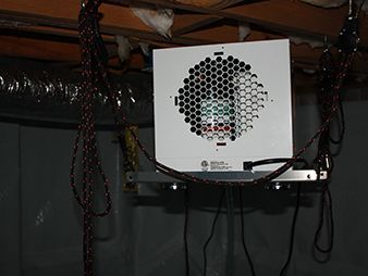 White boxy device with a honeycomb front pattern mounted under a shelf, with cables hanging below