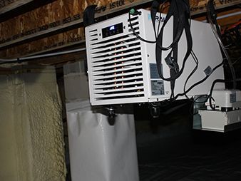 Ceiling-mounted white appliance with vents and hanging cables in a basement-like space