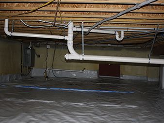 Crawlspace under floor joists with white PVC plumbing and ductwork, lined with reflective insulation.