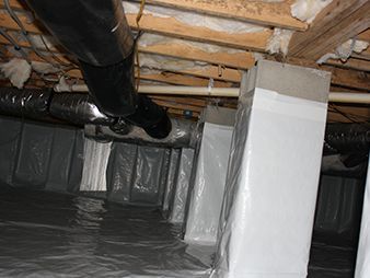 Crawlspace with insulated ducts, white support posts, and plastic moisture barrier under exposed wooden joists