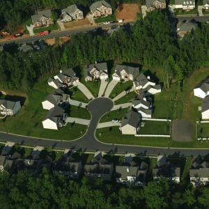Aerial view of a cul-de-sac neighborhood with gray-roofed houses surrounded by trees and roads.