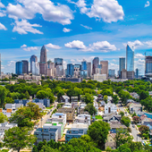City skyline with modern skyscrapers above leafy residential neighborhoods under a bright blue sky