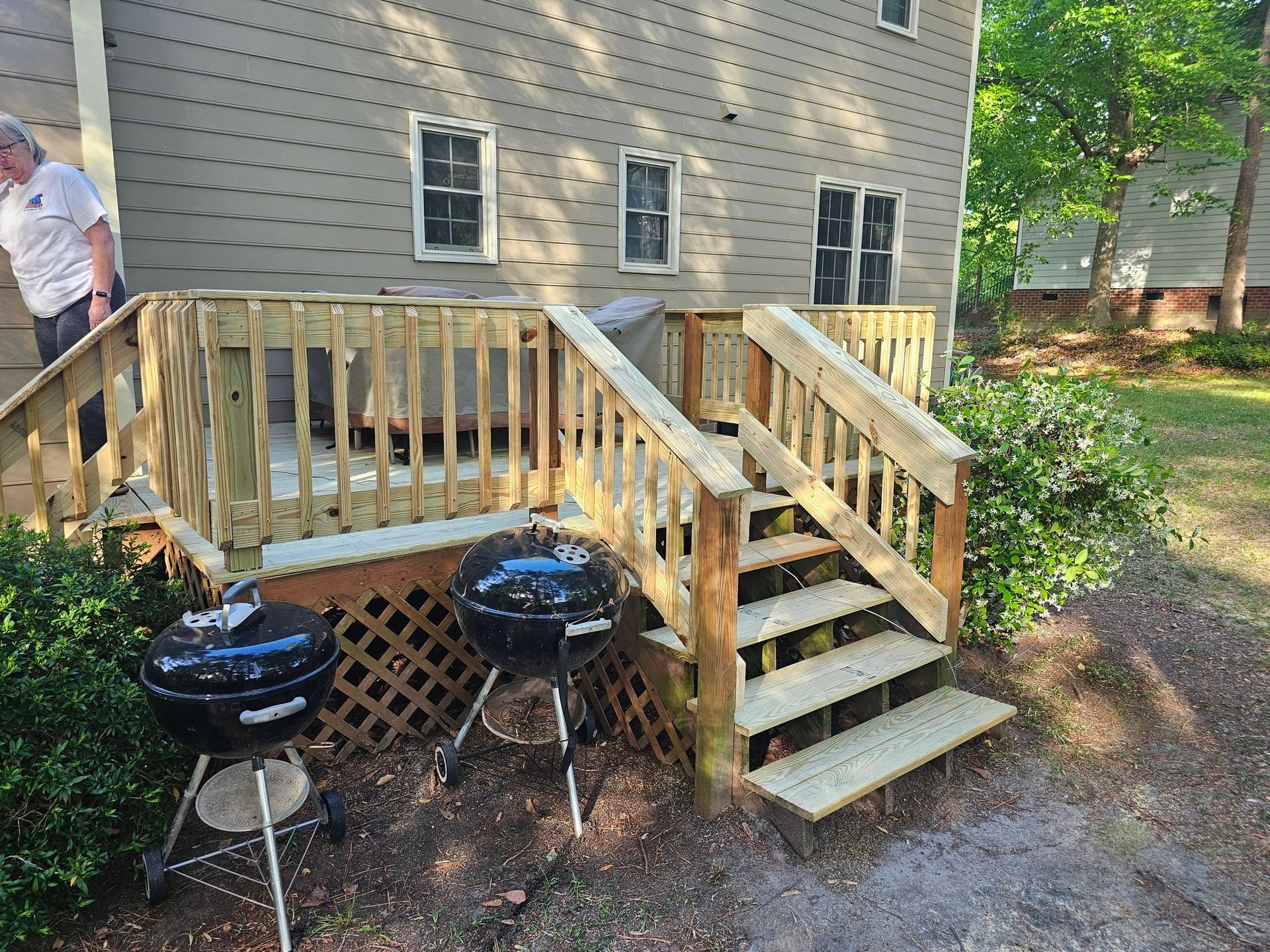 Backyard deck with wooden stairs, lattice skirting, two charcoal grills, and a person at the left edge