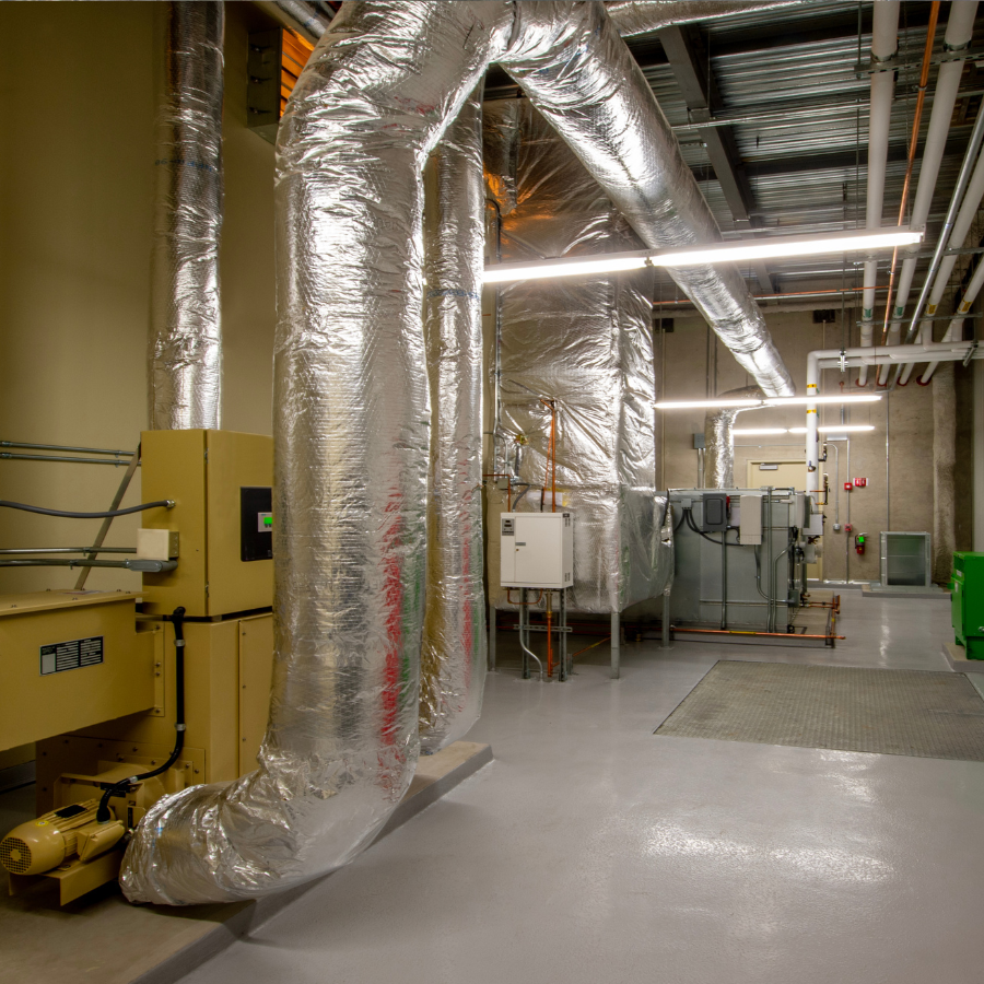 Industrial utility room with large silver ductwork, yellow equipment, and a concrete floor