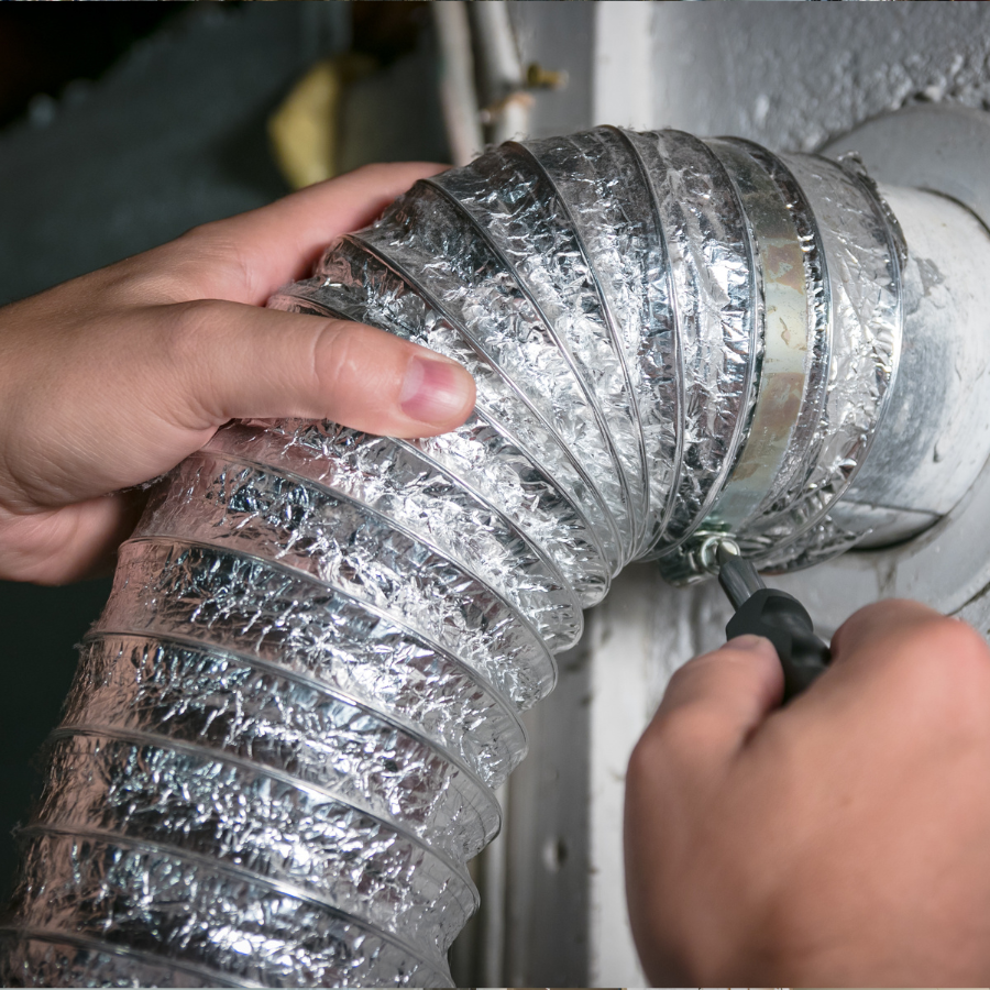 Hands tightening a metal clamp on a silver flexible vent duct attached to a wall.