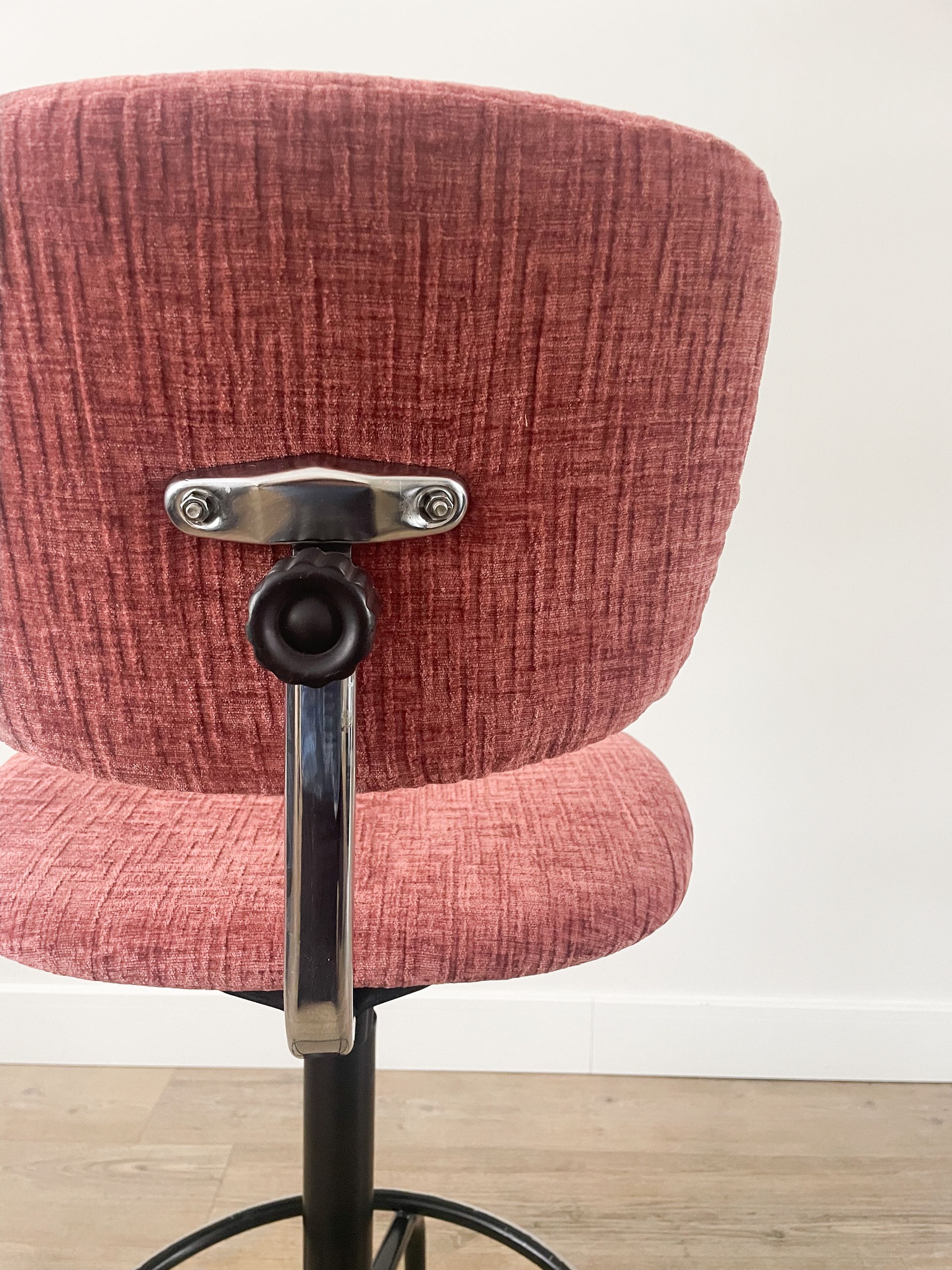 Close-up van de rugleuning van een roze gestoffeerde draaistoel met een zwarte metalen steun in een kamer.