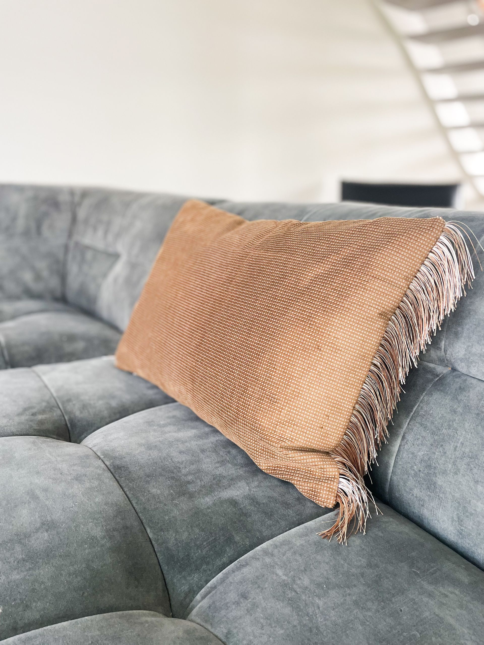 Grijze gecapitonneerde bank met een beige geweven kussen in een lichte woonkamer.