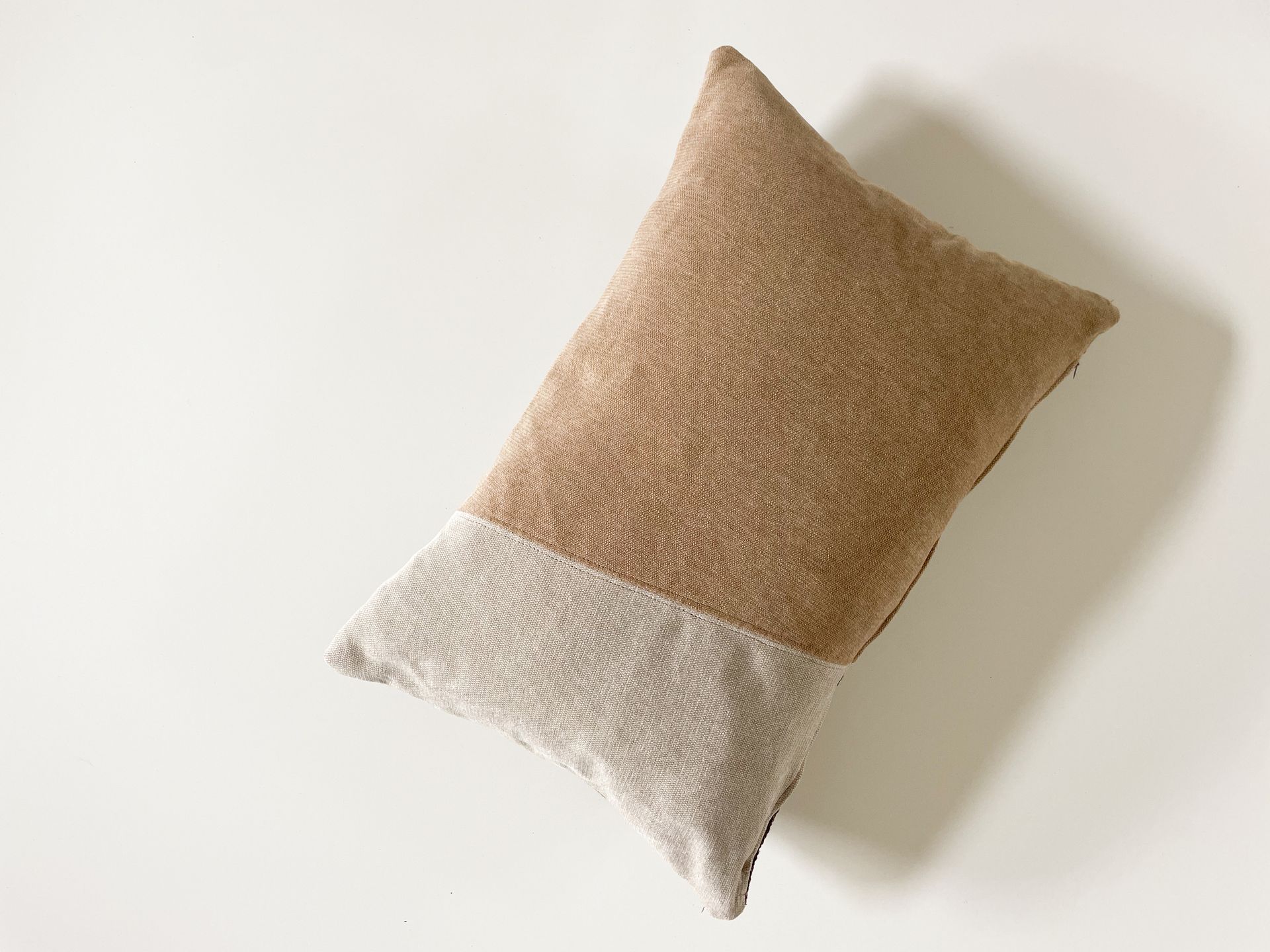 Tweekleurig geweven sierkussen, beige en gebroken wit, op een witte achtergrond.