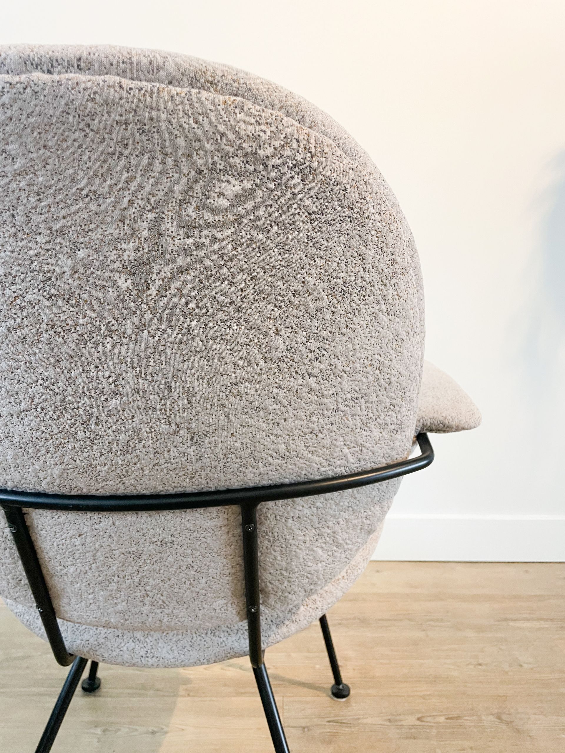 Beige stoel met structuur, zwarte poten en een klein bijzettafeltje op een lichte houten vloer tegen een witte muur.