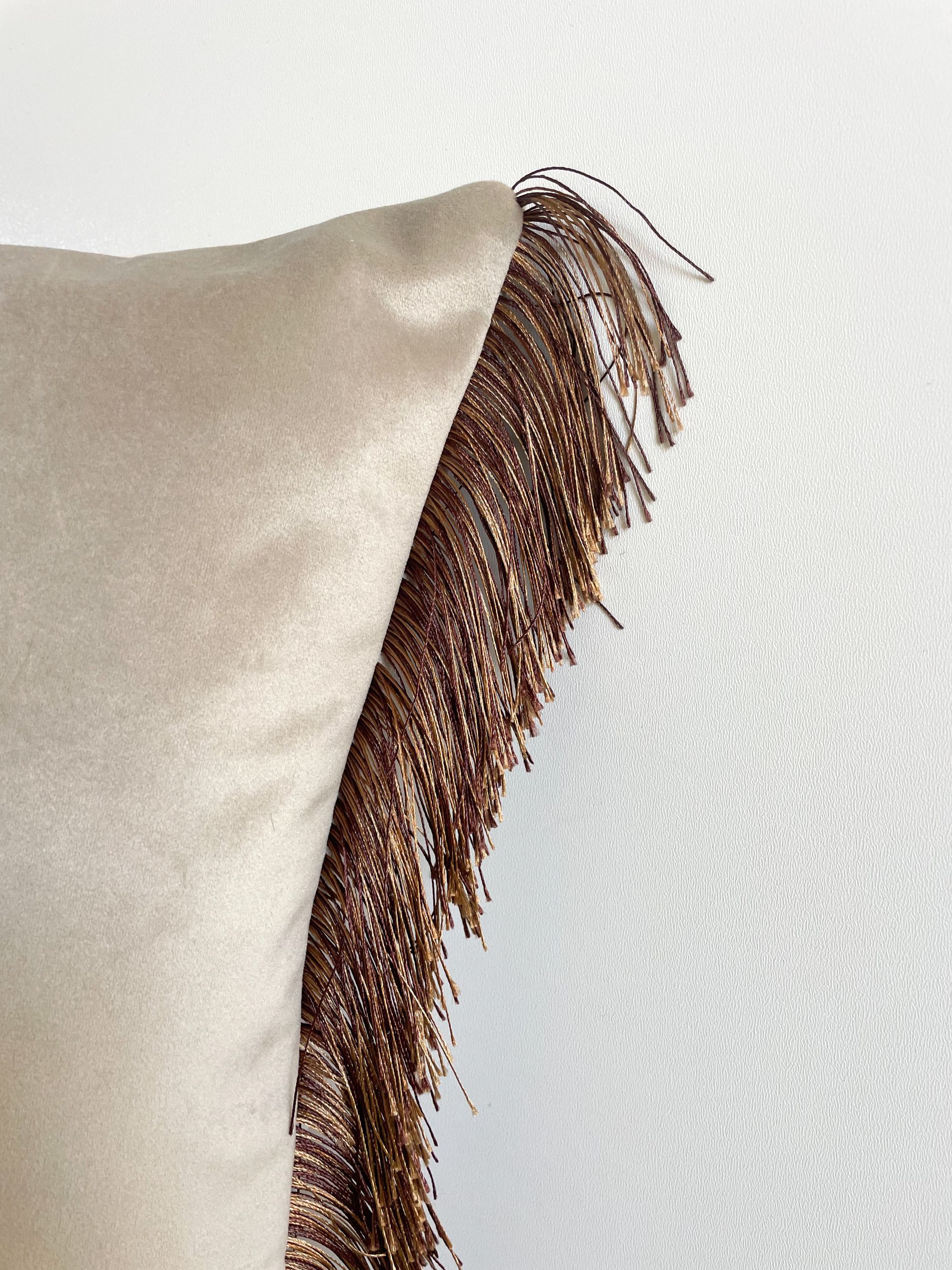 Beige kussen met bruine franjes op een lichte achtergrond.