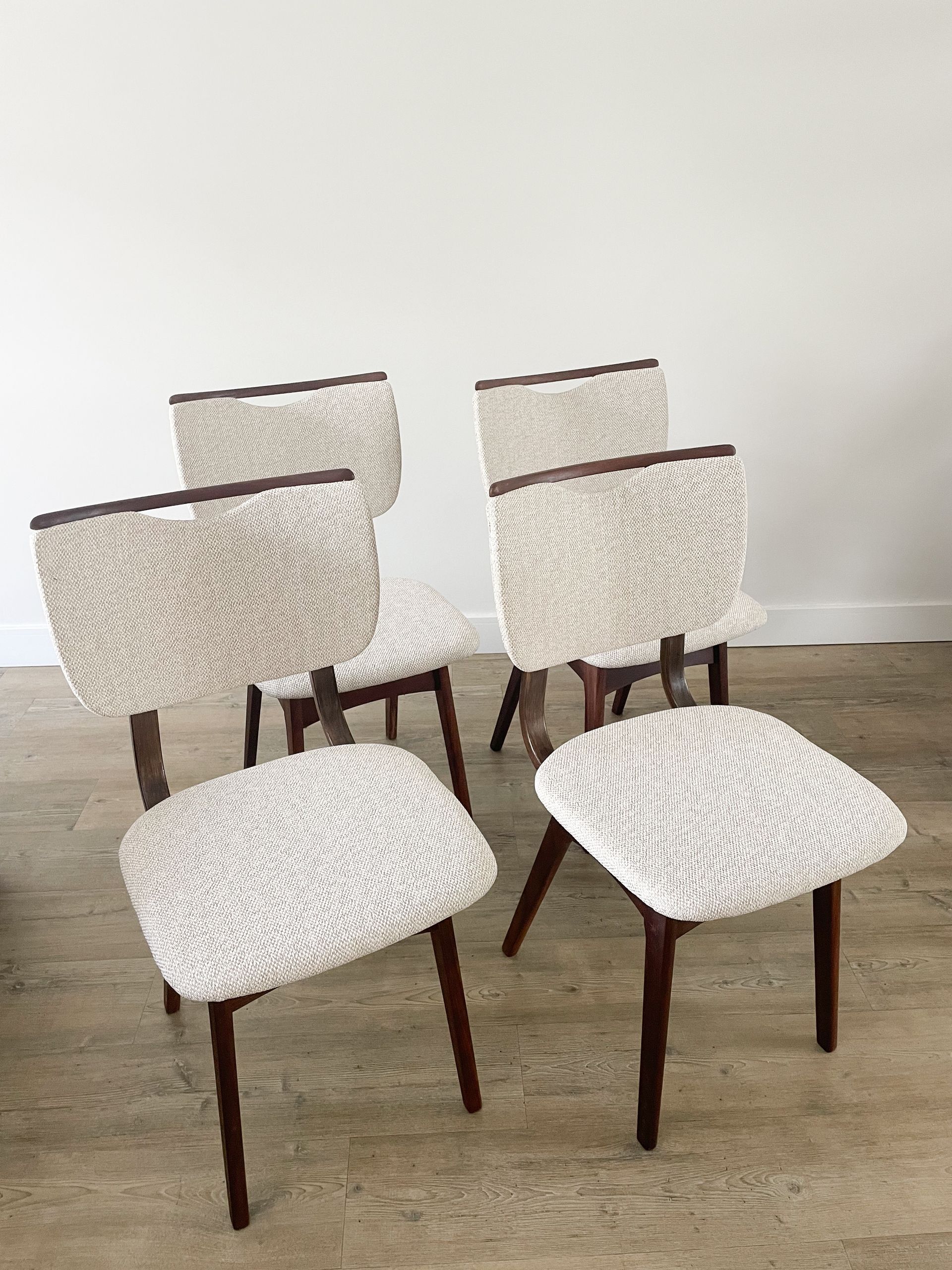 Vijf gestoffeerde eetkamerstoelen met donkerhouten poten staan ​​opgesteld op een betonnen vloer tegen een effen muur.