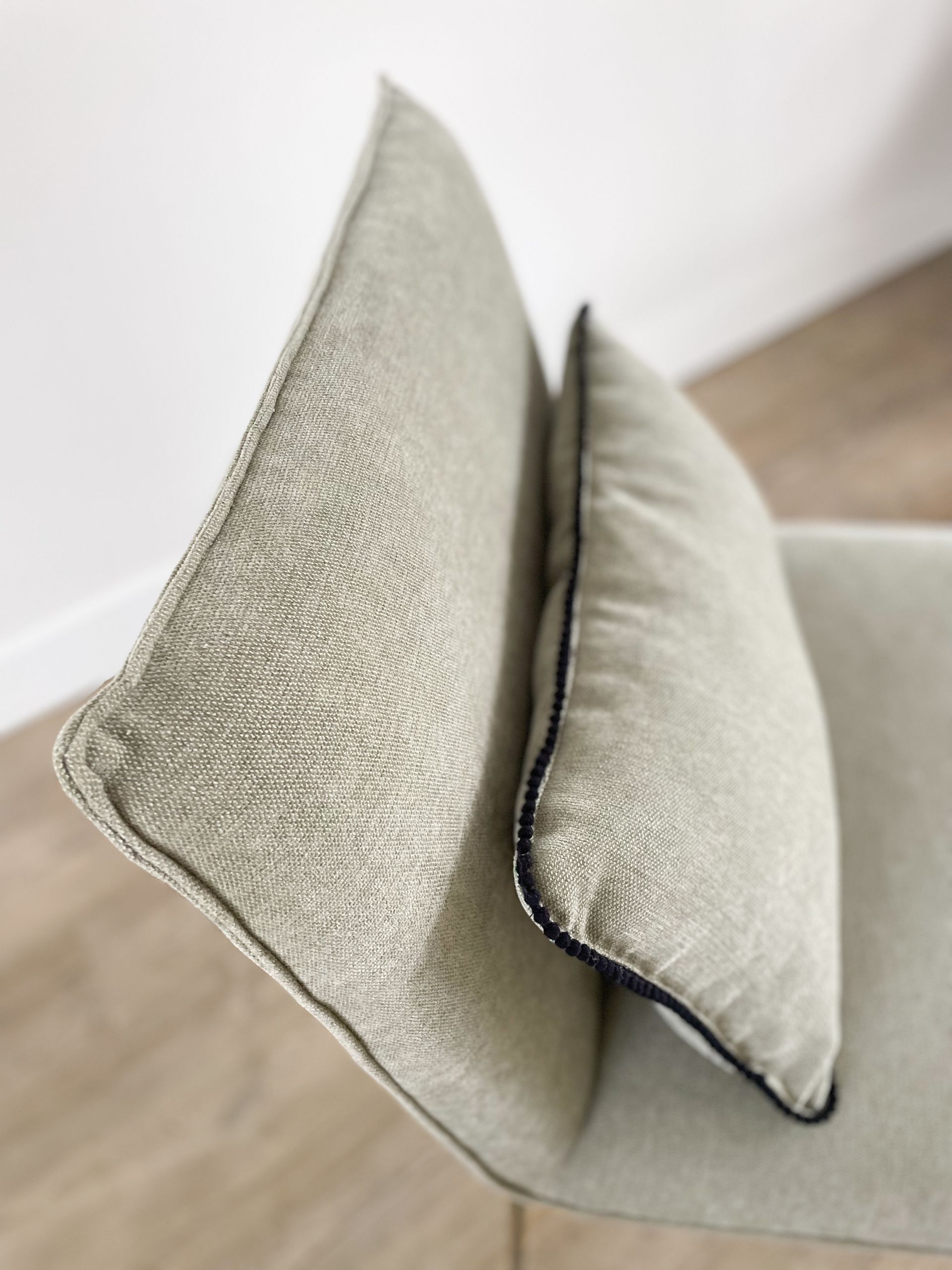 Twee lichtbeige sierkussens met een structuurstof staan ​​tegen een muur op een houten vloer.