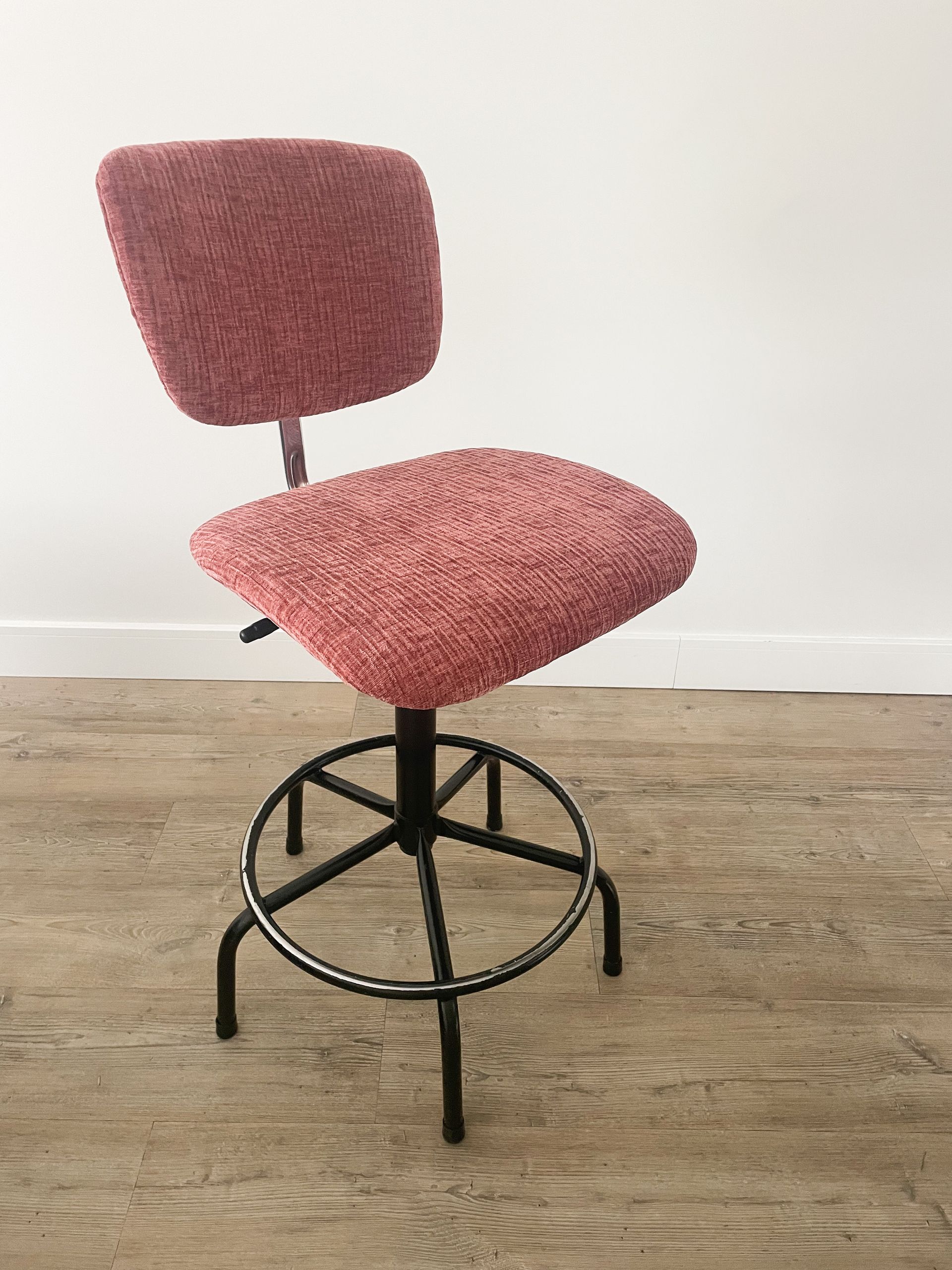 Roze gestoffeerde draaibare barkruk met rugleuning op een houten vloer tegen een witte muur.