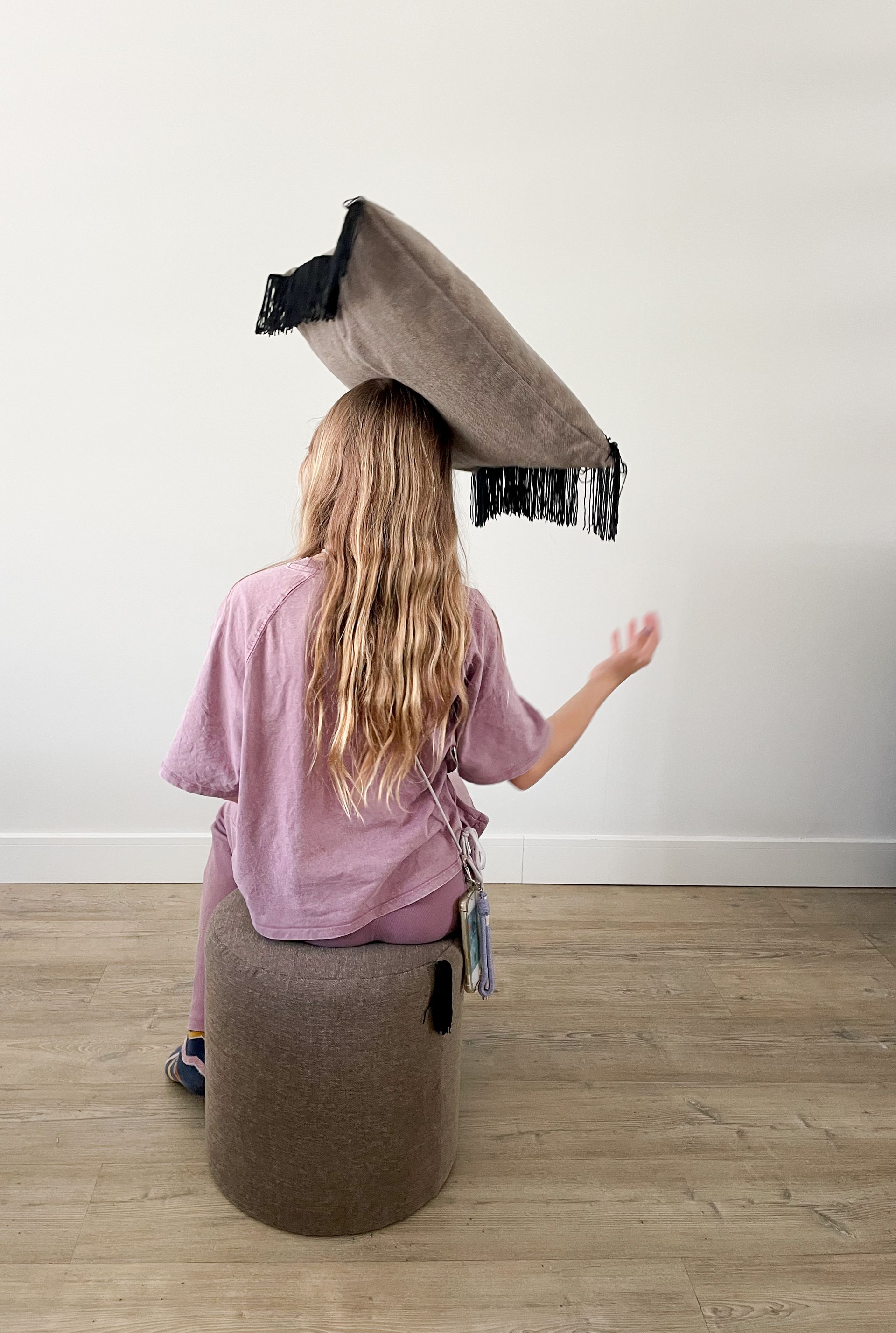 Beige geweven cilindervormige poef op een lichte houten vloer tegen een witte muur.