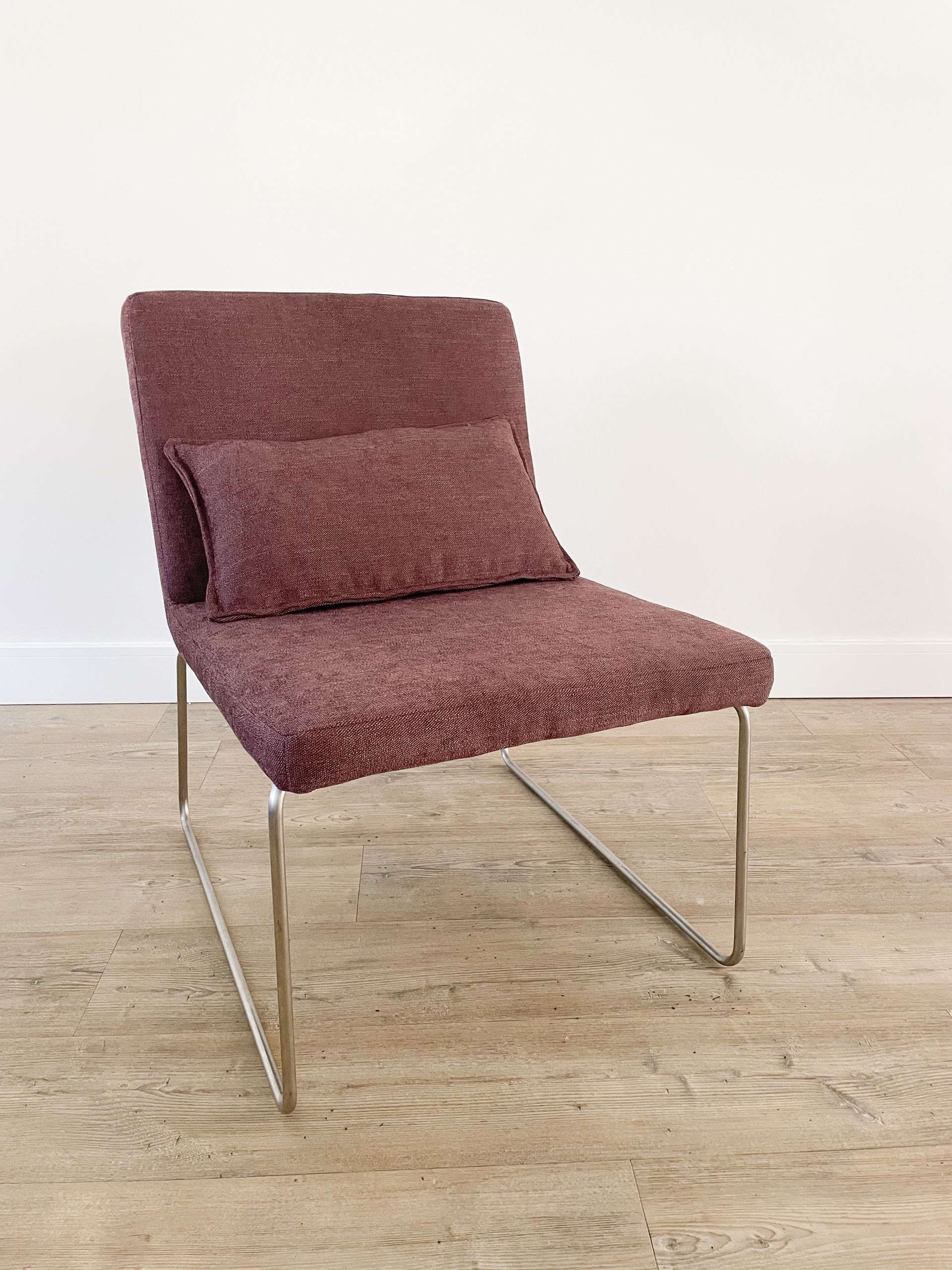 Moderne mauve loungestoel met metalen poten op een lichte houten vloer tegen een witte muur.