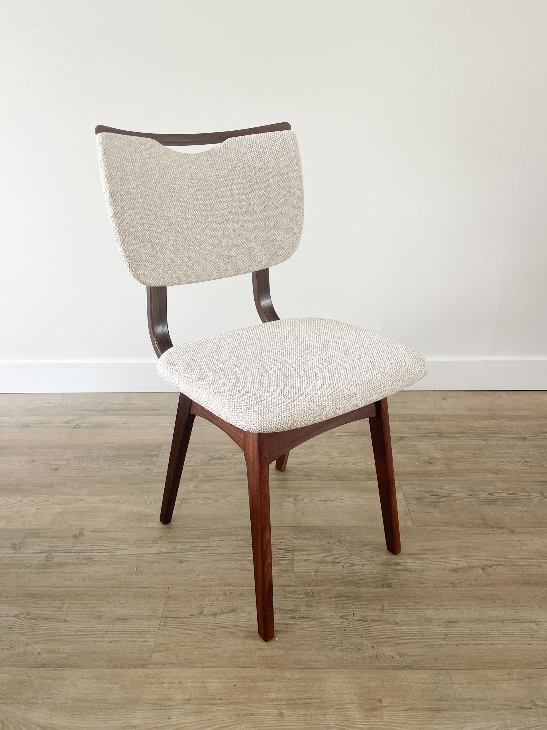 Moderne gestoffeerde stoel met houten poten en een witte, gestructureerde zitting en rugleuning tegen een effen muur.