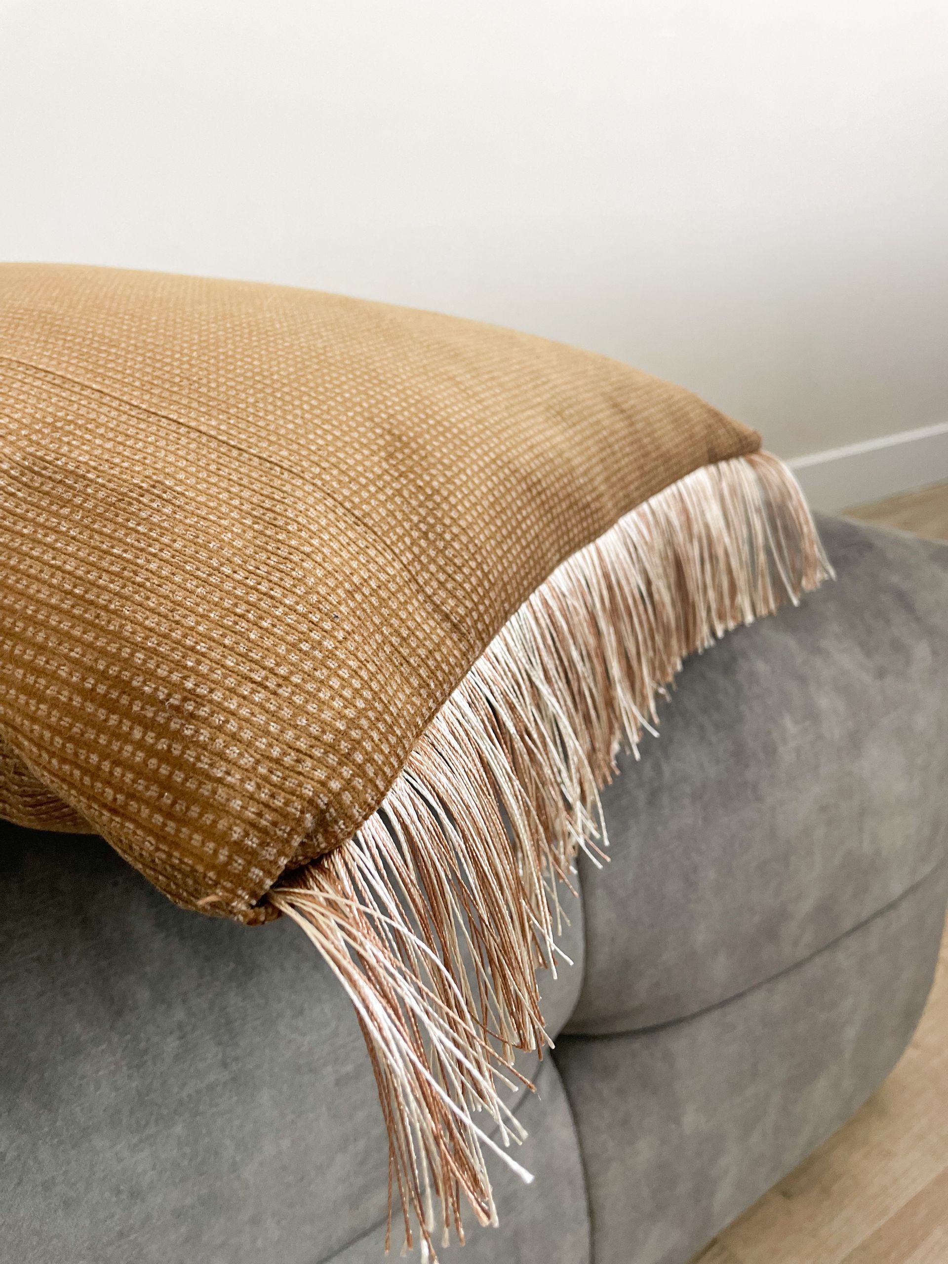 Grijze gecapitonneerde bank met een beige geweven kussen in een lichte woonkamer.