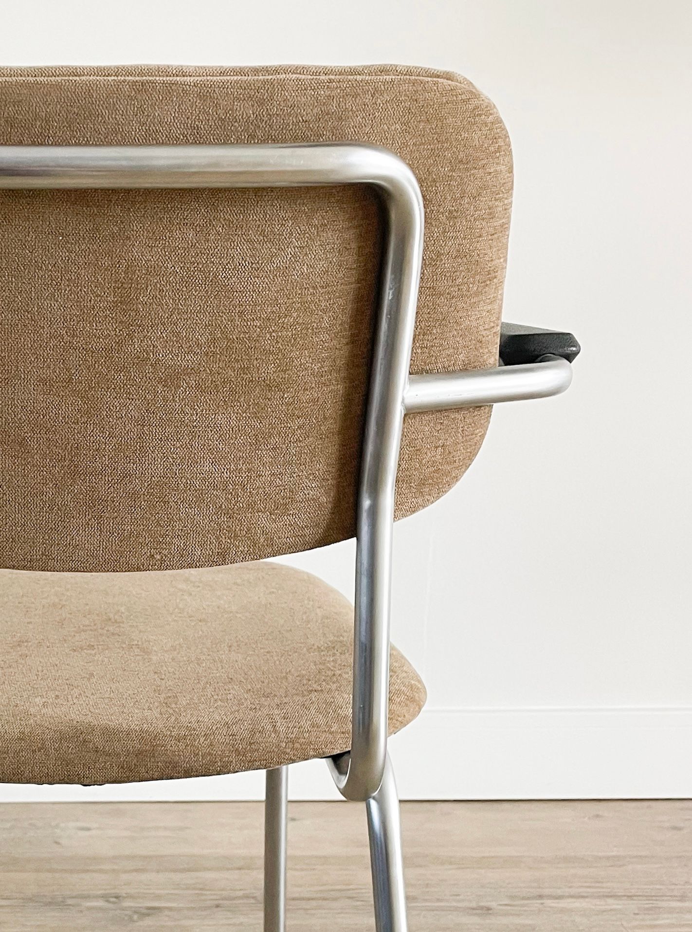 Detailopname van een beige geweven stoel met een zilverkleurig metalen frame op een lichte houten vloer.