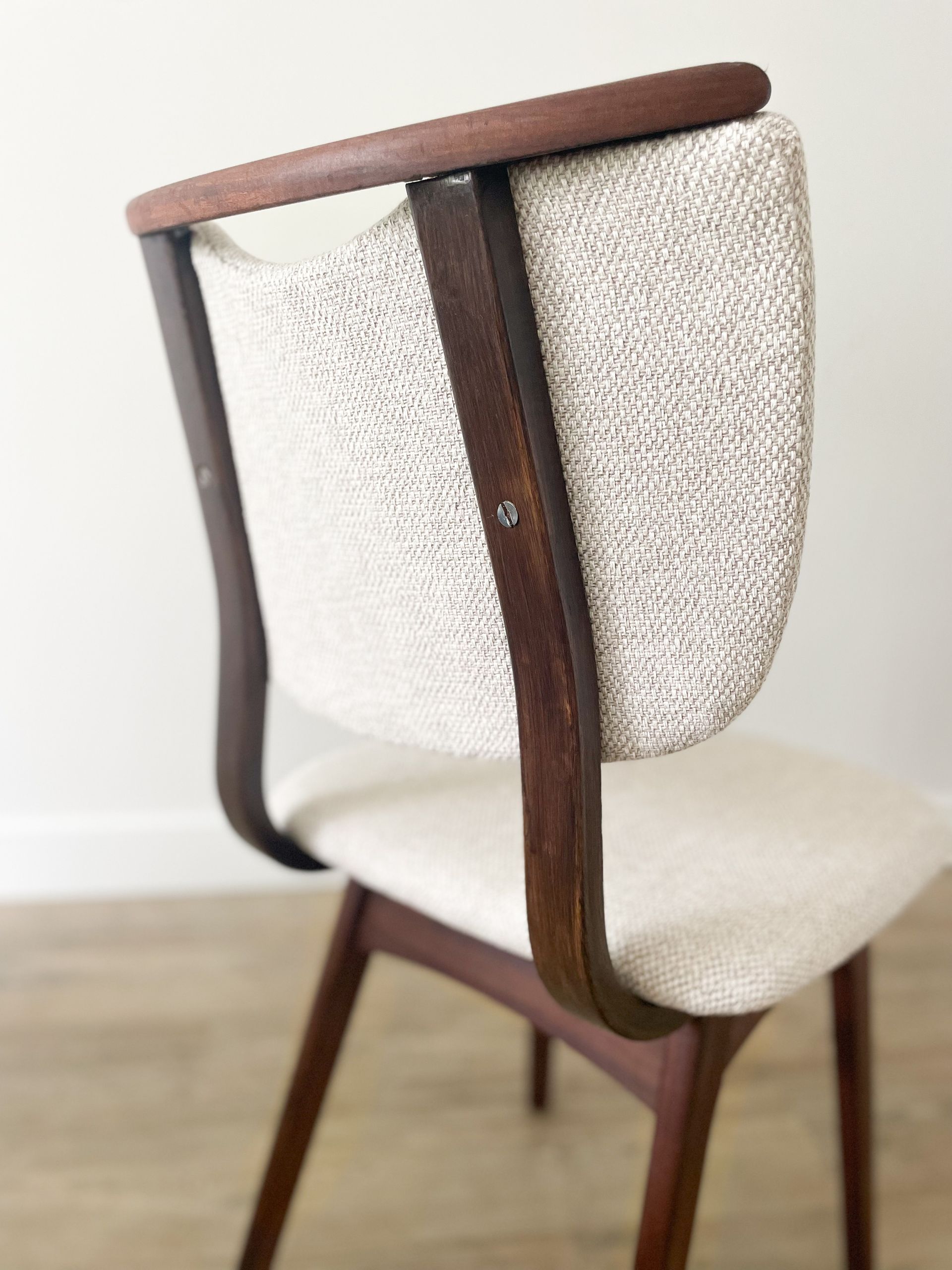 Detailopname van een houten stoel met een beige gestoffeerde zitting en een witte, gestructureerde rugleuning.