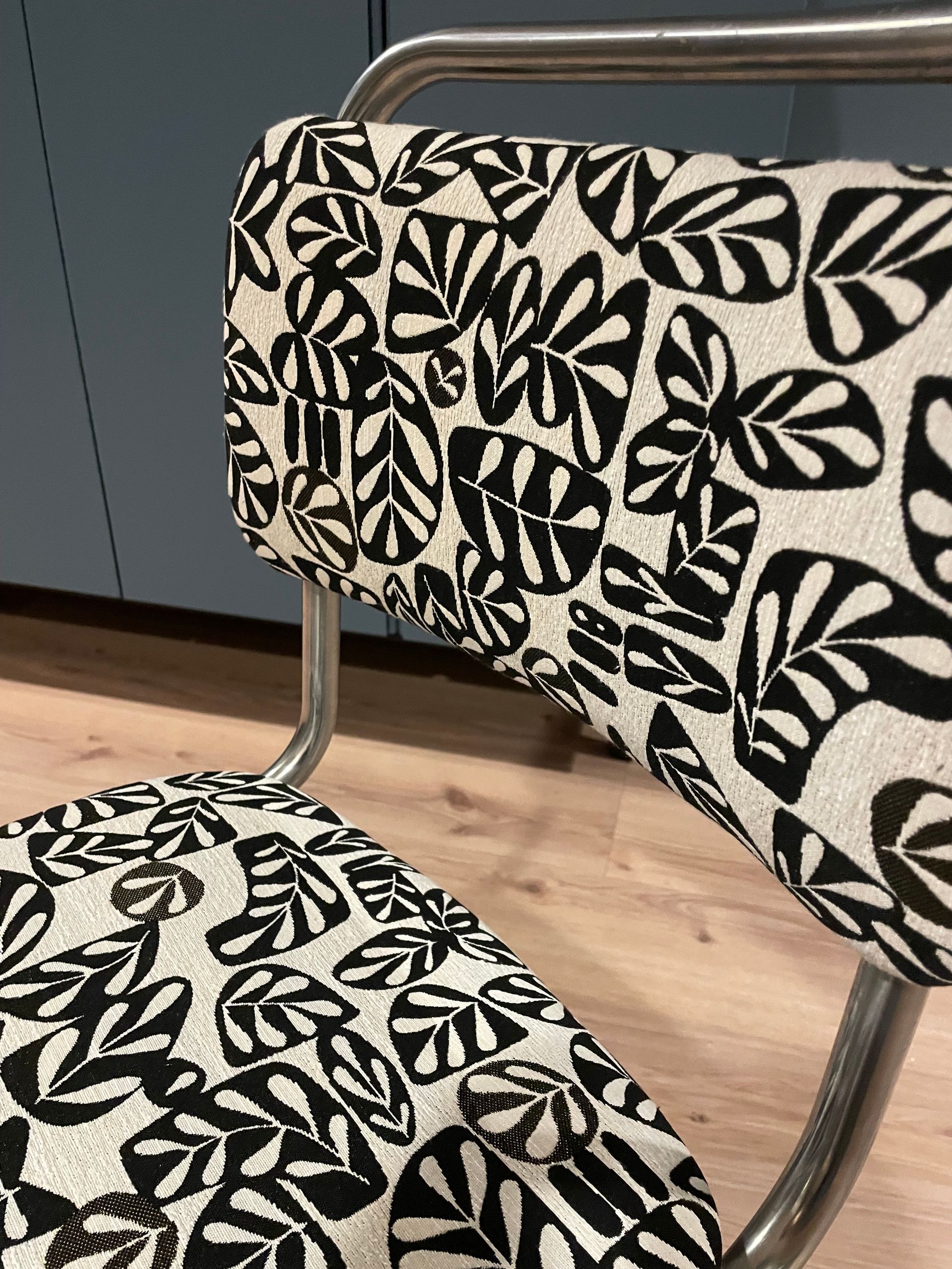 Een zwart-wit gestreepte gestoffeerde stoel en een bijpassende kruk op een houten vloer binnenshuis.