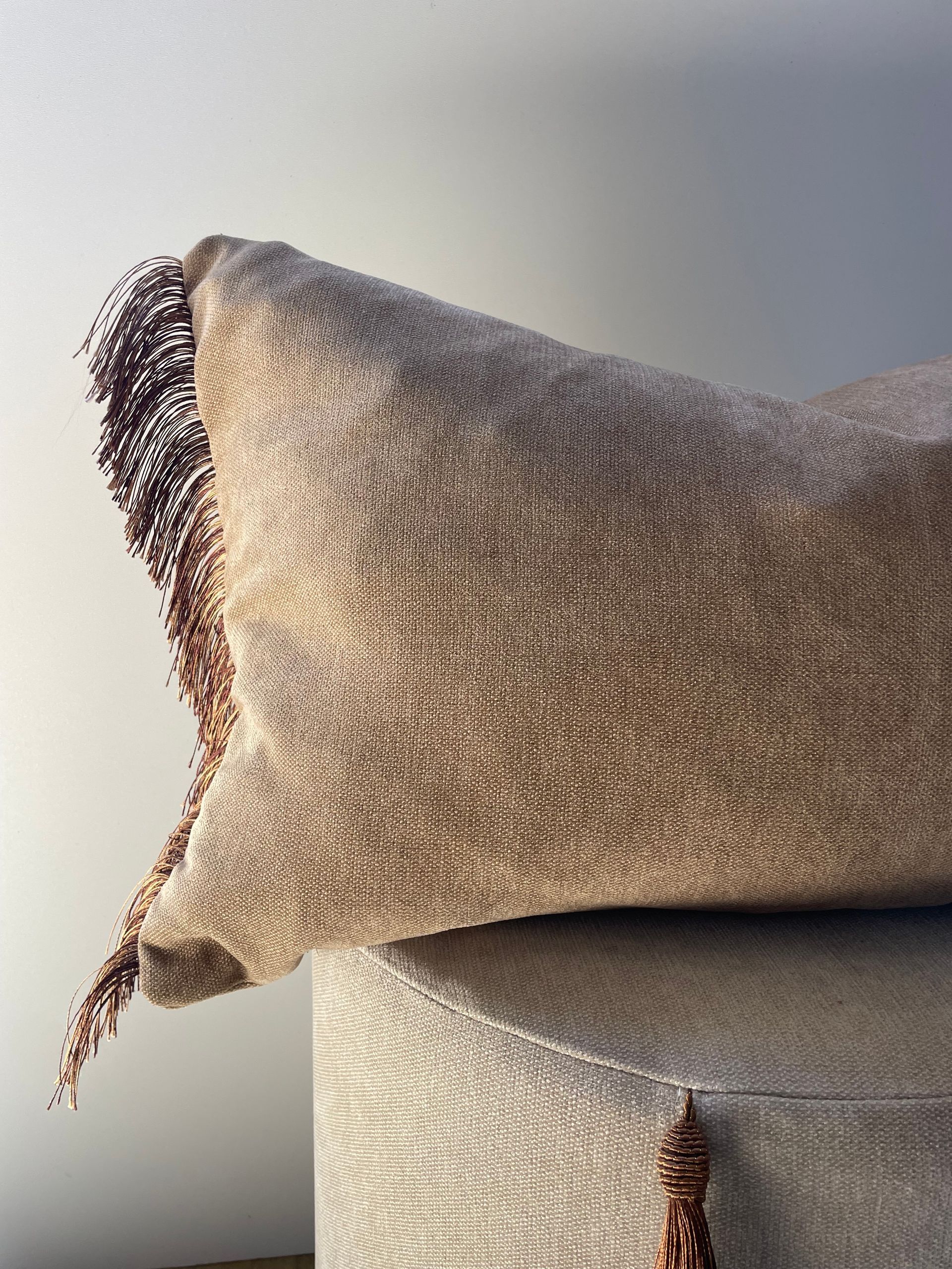 Beige kussen met textuur op een lichte bank tegen een witte muur.