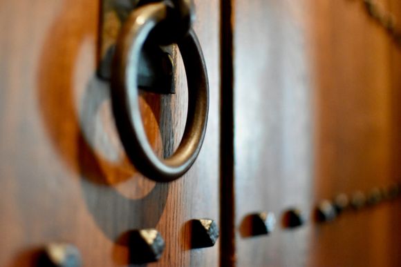 A close-up of a metal ring handle on a dark wood door featuring decorative metal studs.