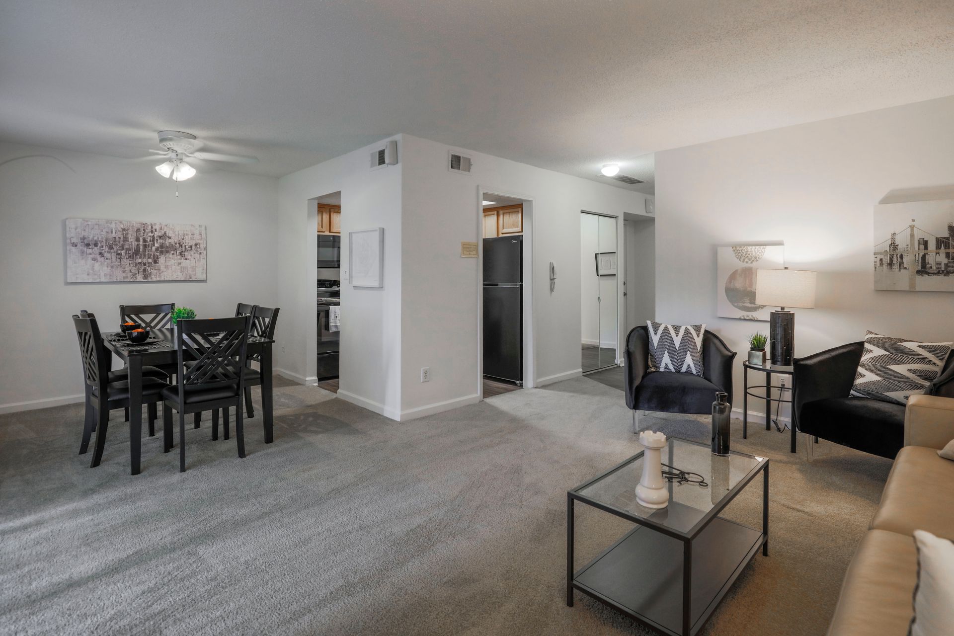 Open-concept living and dining room with gray carpet, black furniture, and white walls