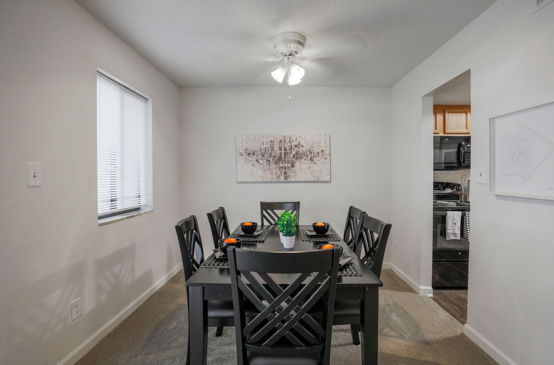Dining room with a black table and chairs, beige carpet, wall art, and a ceiling fan.