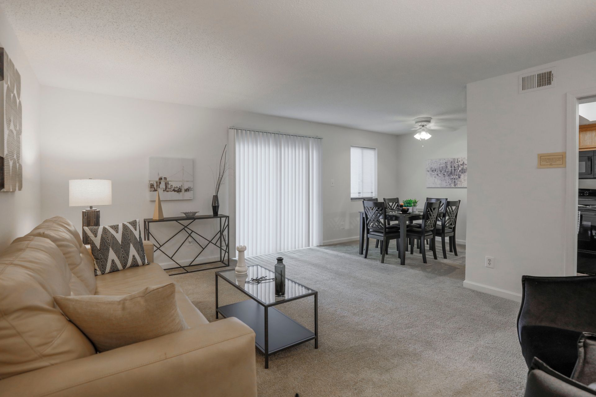 Bright living room with beige sofa, gray carpet, glass coffee table, and dining area by sliding doors