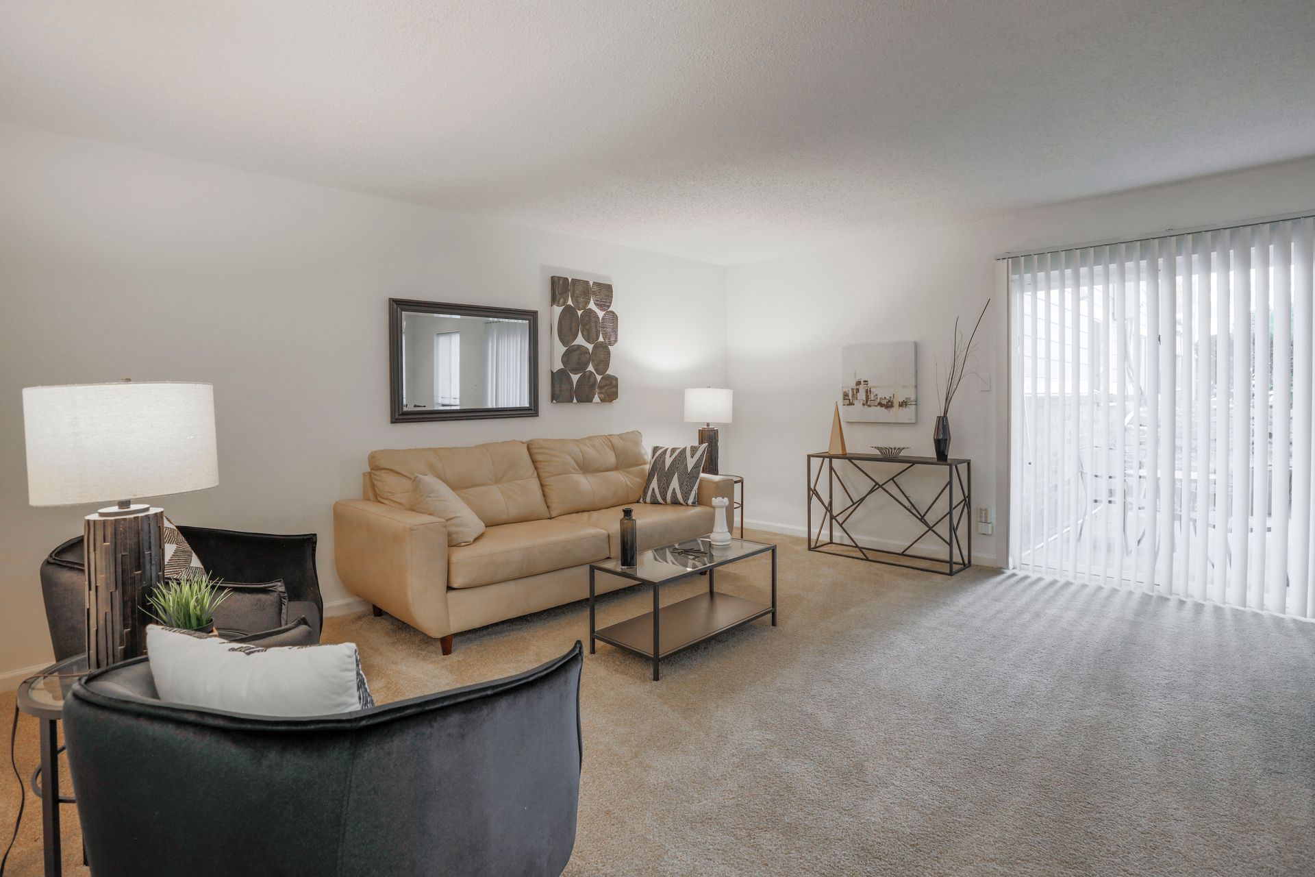 Bright living room with beige sofa, black chairs, glass coffee table, and vertical blinds