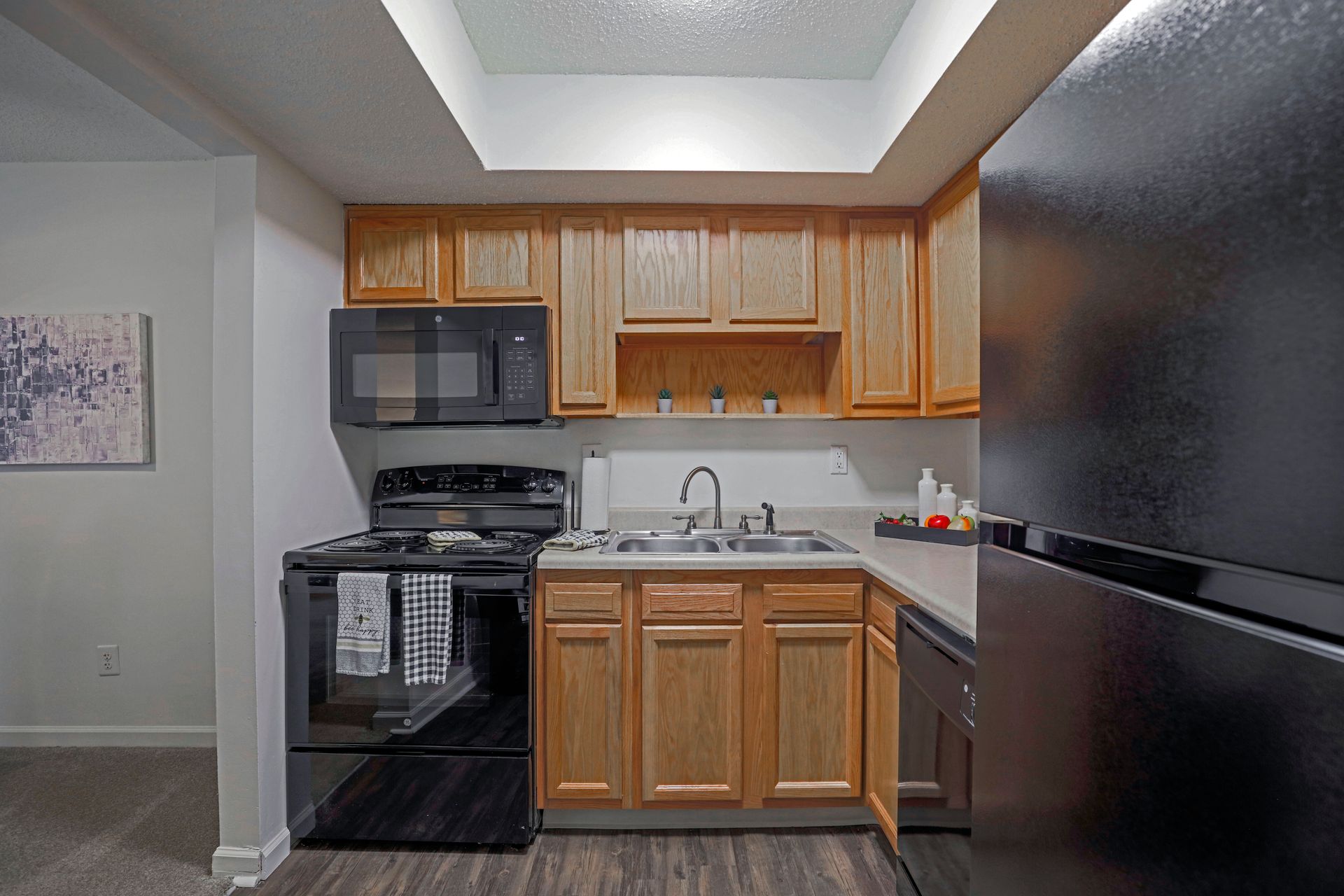 Compact kitchen with wood cabinets, black appliances, and a white sink under bright ceiling light