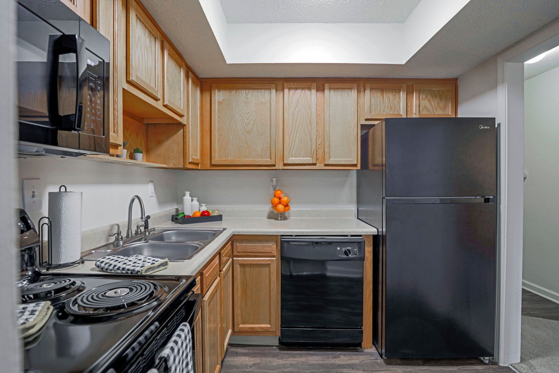 Small kitchen with wooden cabinets, black appliances, and a sink under a skylight.