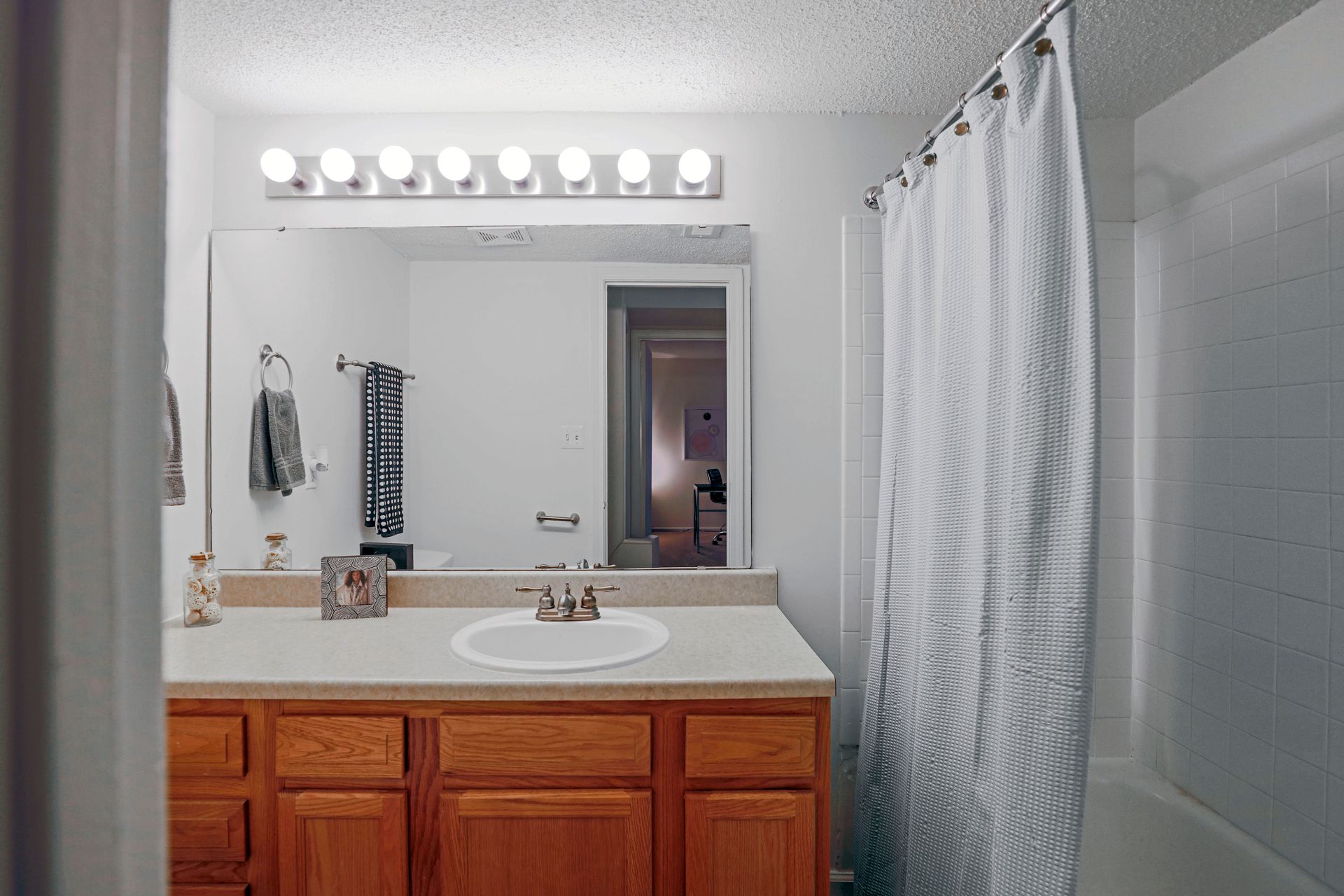 Bathroom with wooden vanity, large mirror, and white shower curtain beside a bathtub.