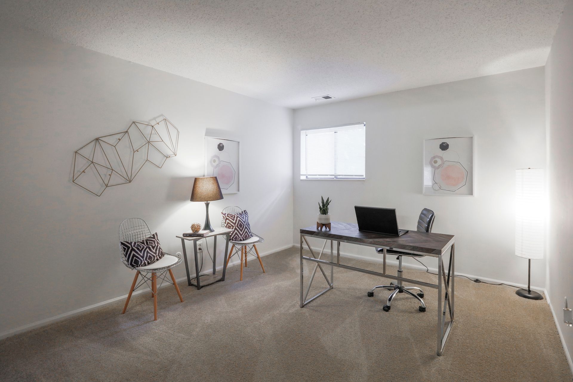 Minimal home office with desk, computer, chair, lamp, wall art, and a couple of chairs by the wall.