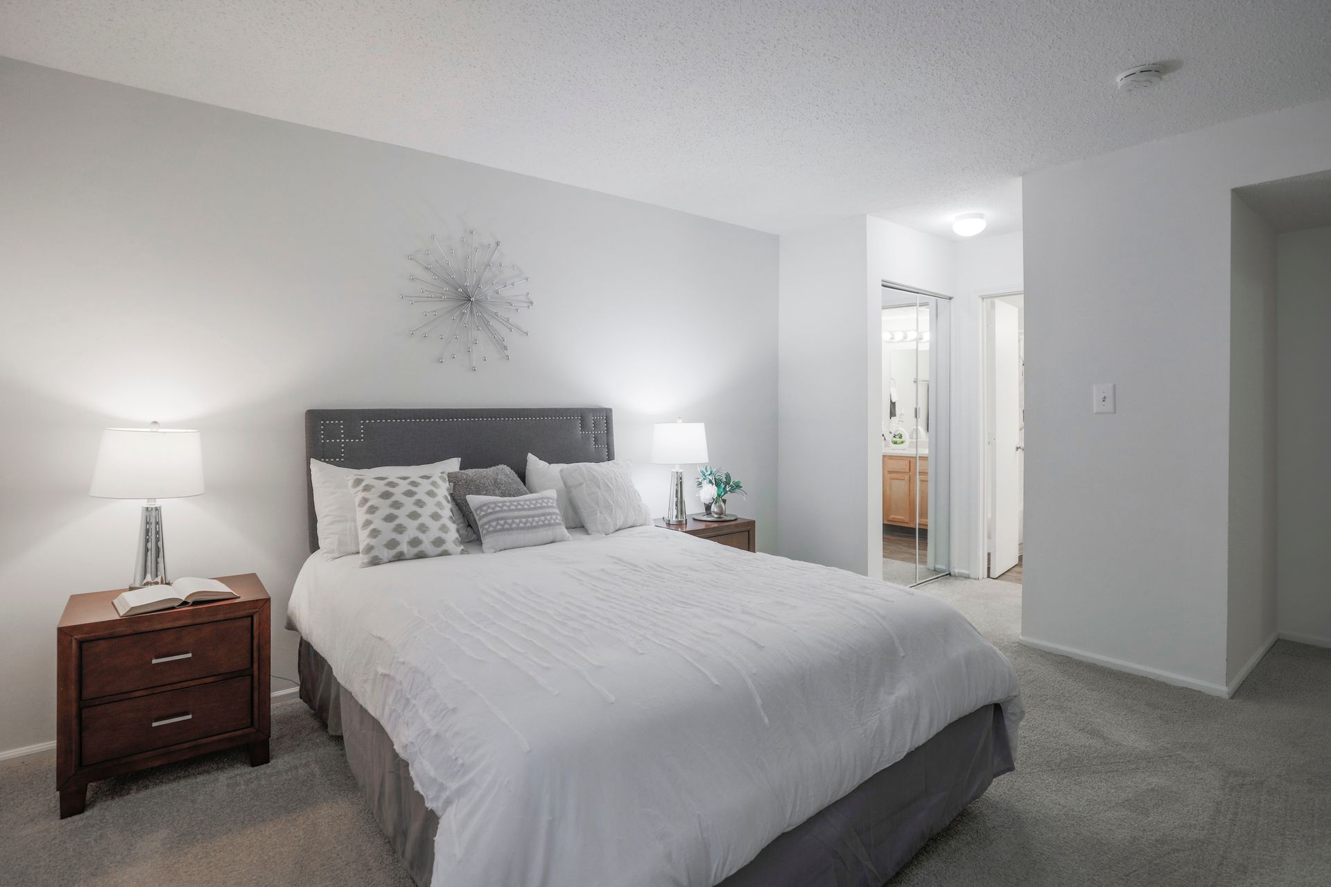 Bright bedroom with a white bed, dark upholstered headboard, nightstands, and an open doorway to a bathroom.
