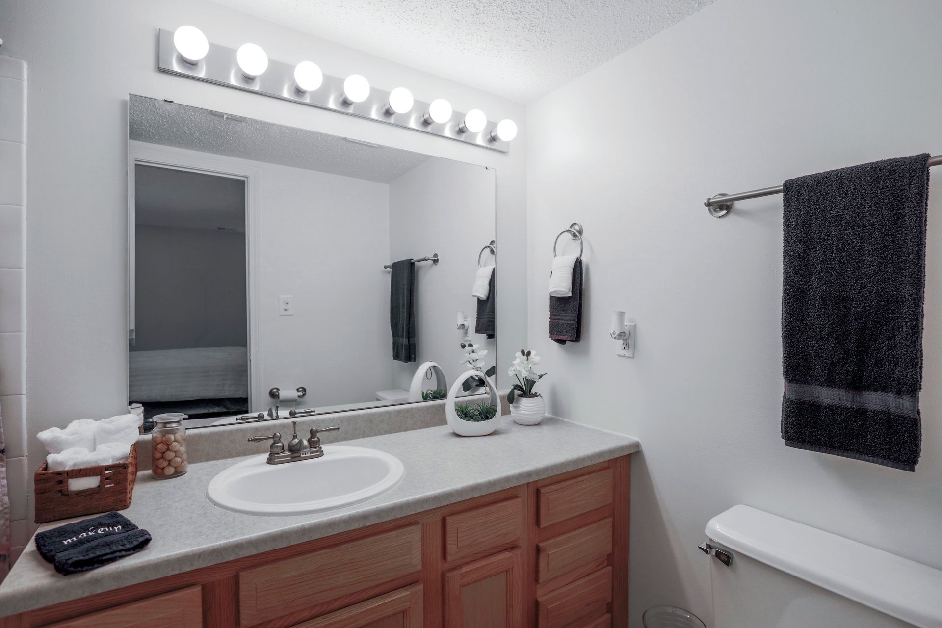 Bright bathroom vanity with mirror lights, sink, towels, and toilet paper holder.