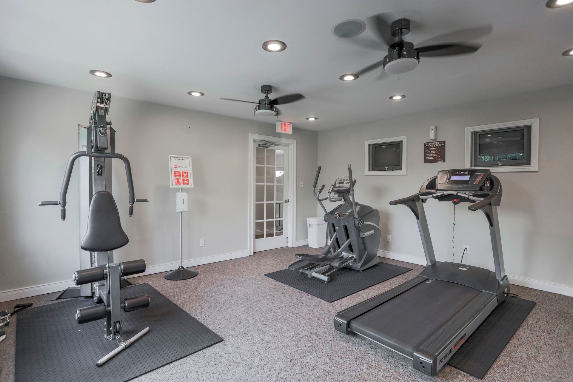 Home gym with weight machine, elliptical, and treadmill on gray carpet in a room with ceiling fans