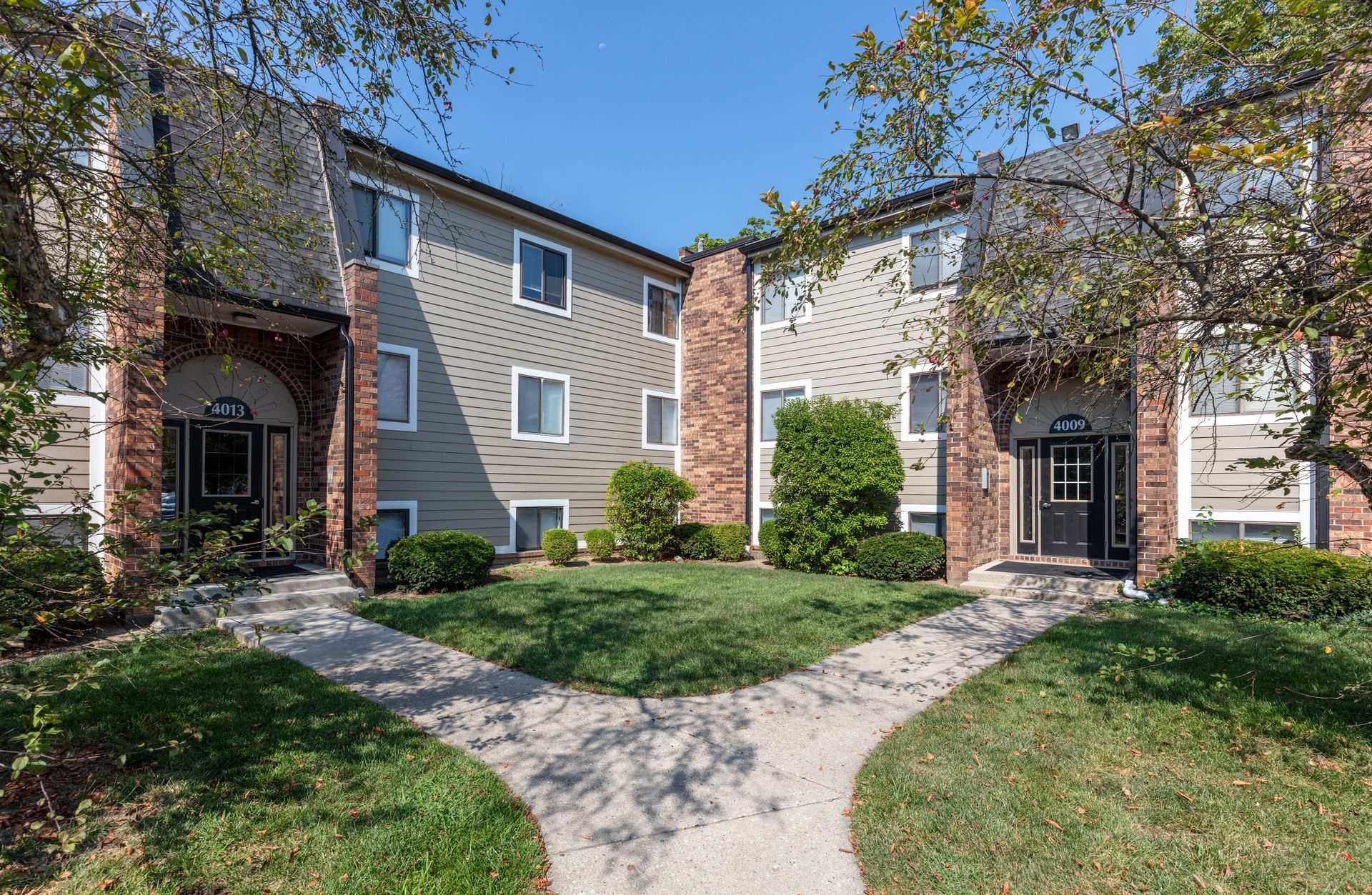 Courtyard of tan apartment buildings with brick accents, trees, and a winding walkway