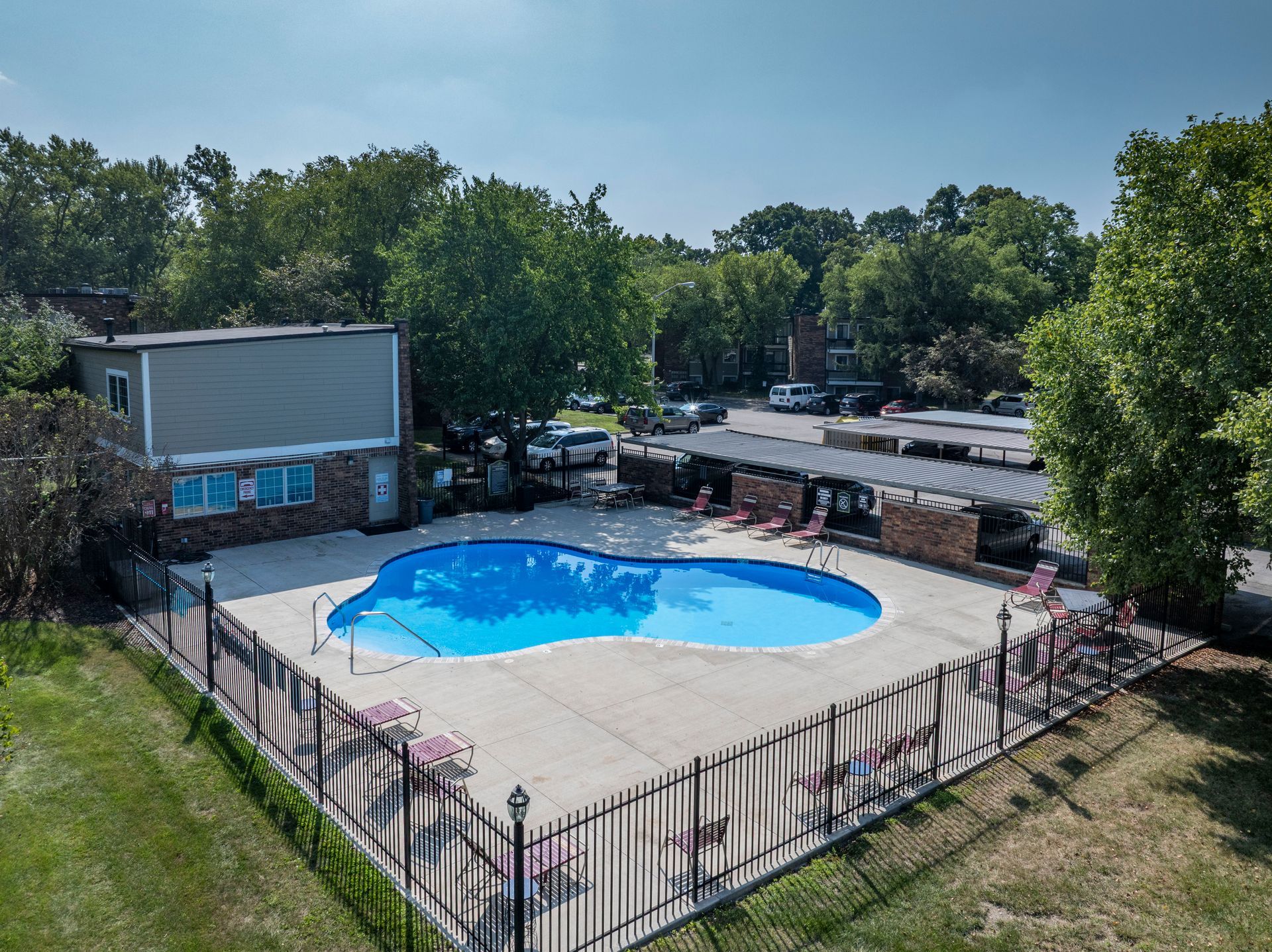 Outdoor swimming pool surrounded by a fence and trees, with a small building and lounge chairs nearby