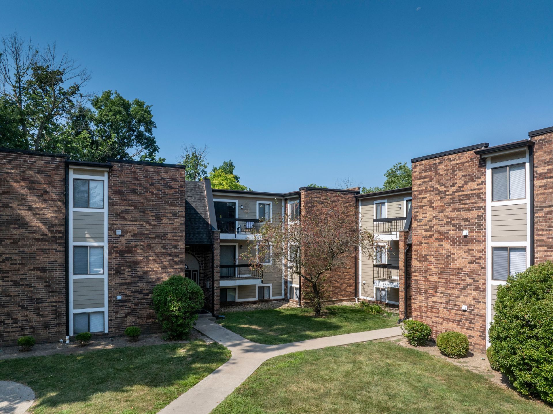 Brick apartment complex with grassy courtyard and trees under a clear blue sky