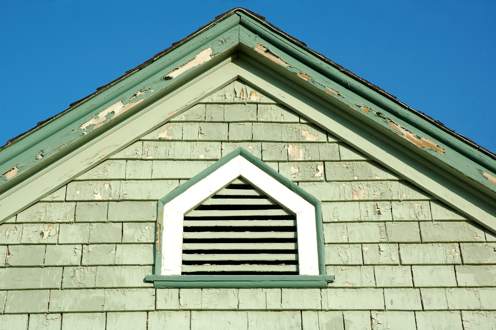 Close-up of a house gable with a small white-trimmed vent and weathered green siding