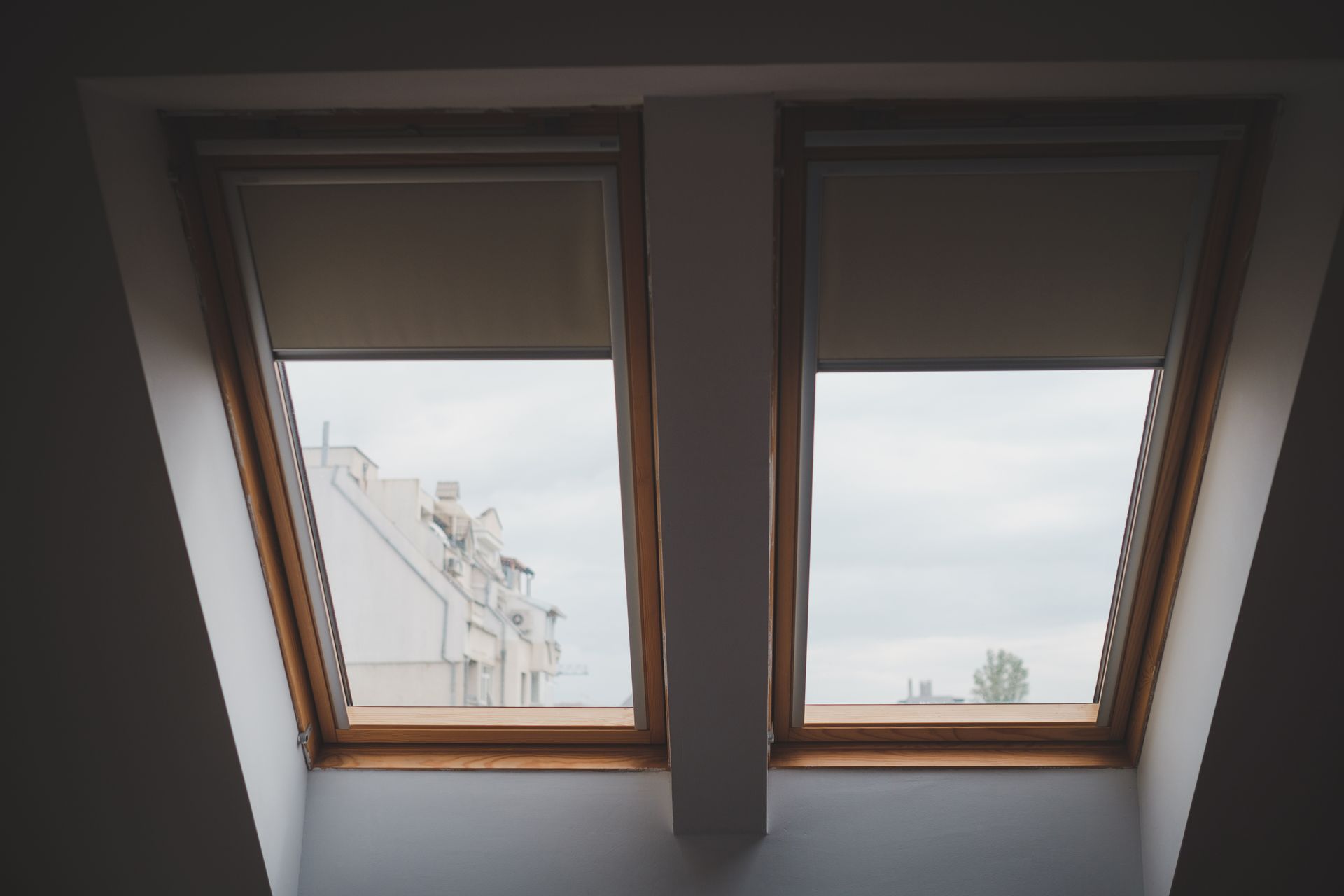 Two skylight windows in a slanted ceiling, showing a cloudy sky and a building outside.